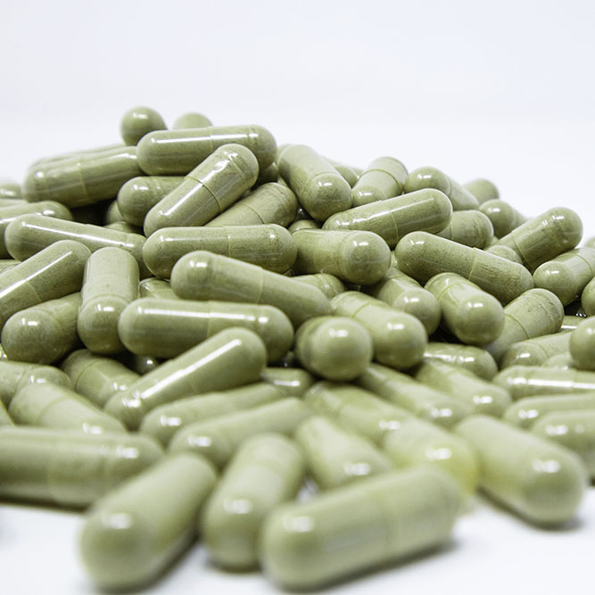 A pile of capsules filled with green Malay kratom powder.