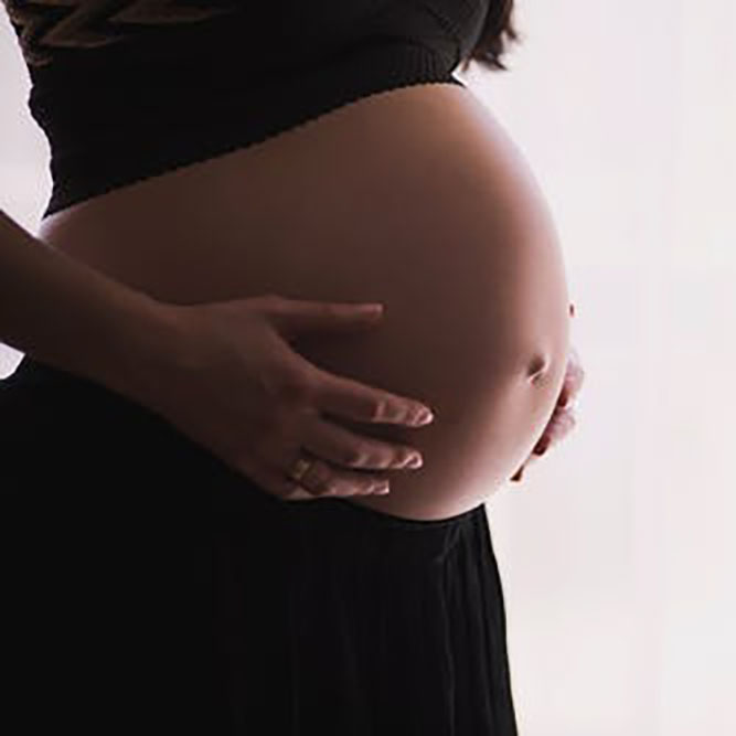 A photo of a pregnant person holding their abdomen.