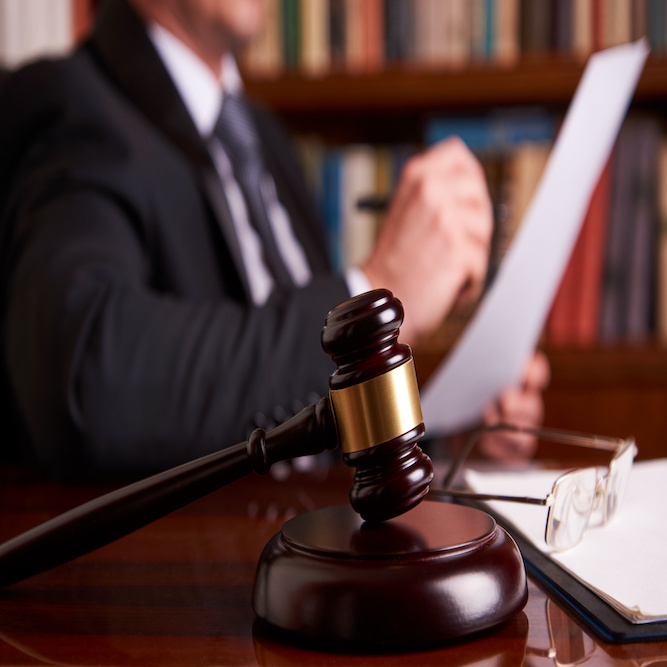 Featured Image depicting a judges gavel resting on a mahogany desk. In the background is the blurred image of a lawyer hard at work fighting the FDA's Kratom Ban