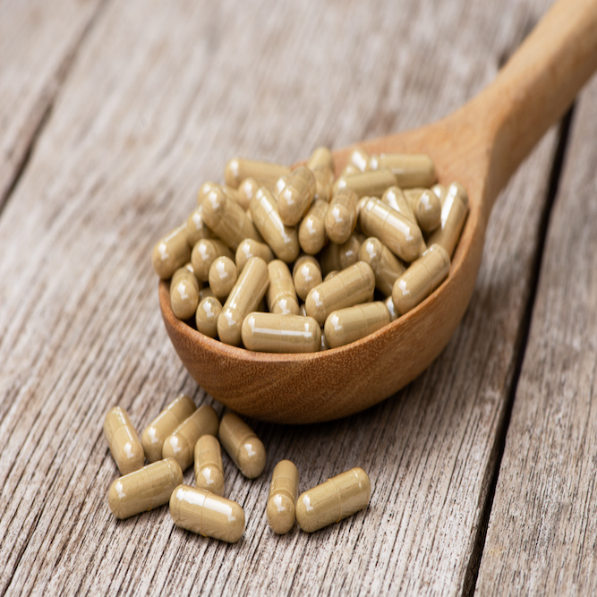 A wooden spoon filled to the point of overflow, with creatum pills (also known as kratom capsules)